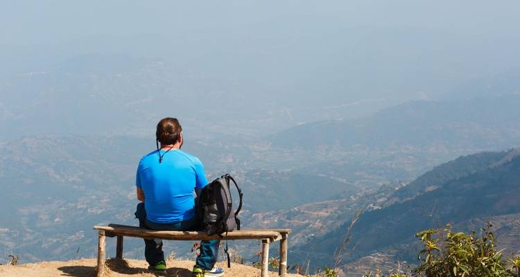 Persoon zittend op een bankje met uitzicht op een vallei.