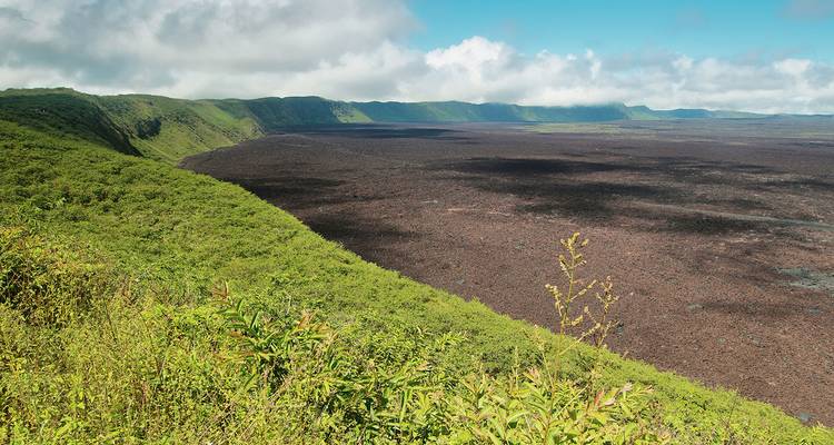 Vista amplia de una vasta caldera volcánica rodeada de acantilados verdes y exuberantes bajo un cielo azul.