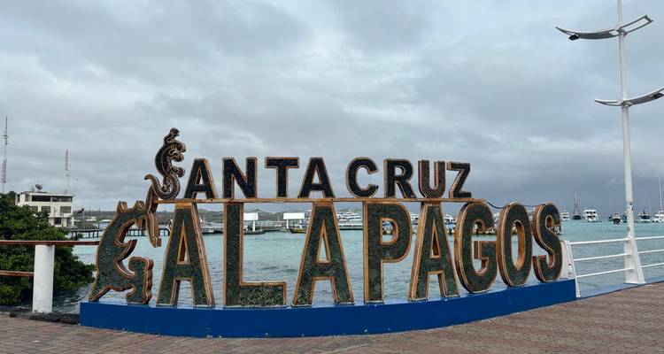 Panneau décoratif « Santa Cruz Galapagos » sur une promenade en bord de mer avec des bateaux en arrière-plan