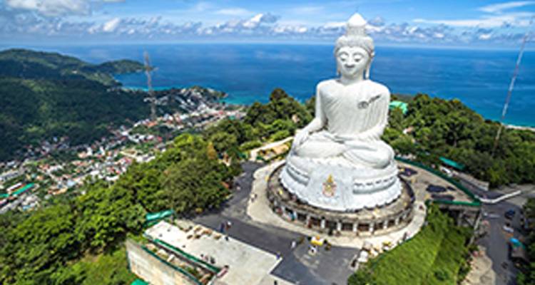 Large white Buddha statue overlooking a coastal town from a hill.