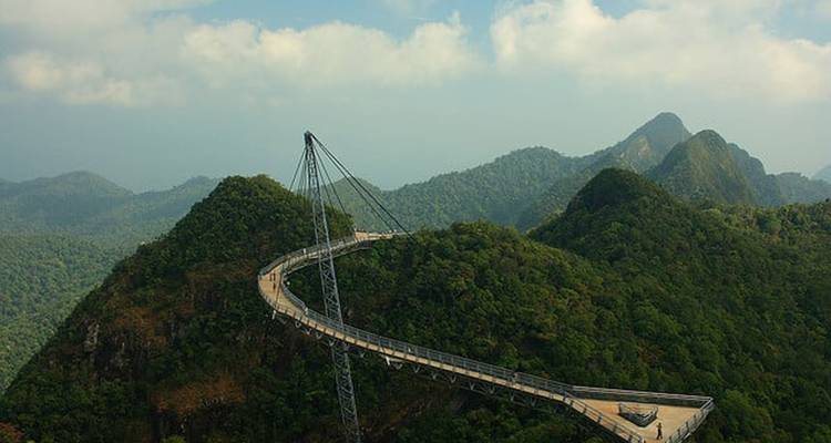 Curved pedestrian bridge extending over lush hills.
