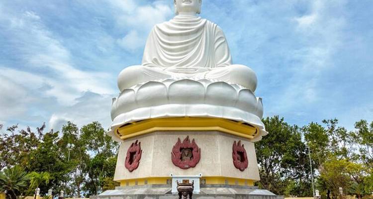 White Buddha statue on a lotus base under a clear blue sky.