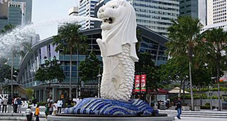 Merlion statue spouting water with city buildings in the background.