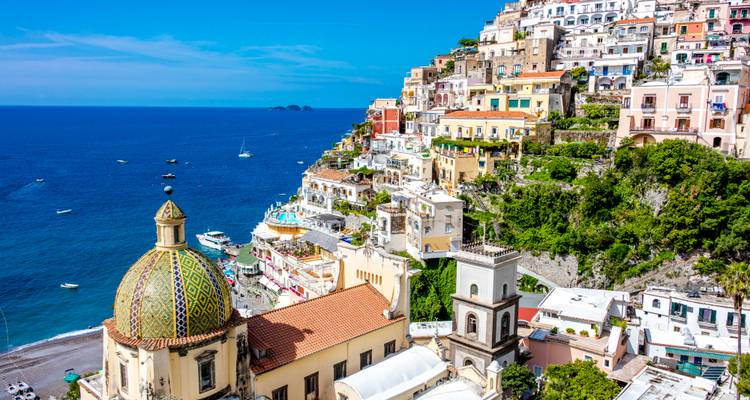 Iconic dome of Santa Maria Assunta and colourful terraced houses of Positano above the blue sea.