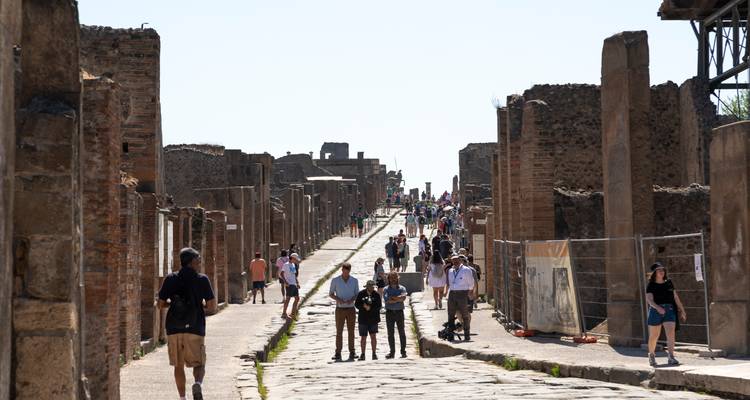 Cobblestone street through the ancient ruins of Pompeii with tourists exploring.