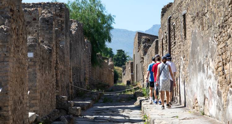 Een rij bezoekers loopt door een smalle stenen steeg tussen de ruïnes van Pompeï.