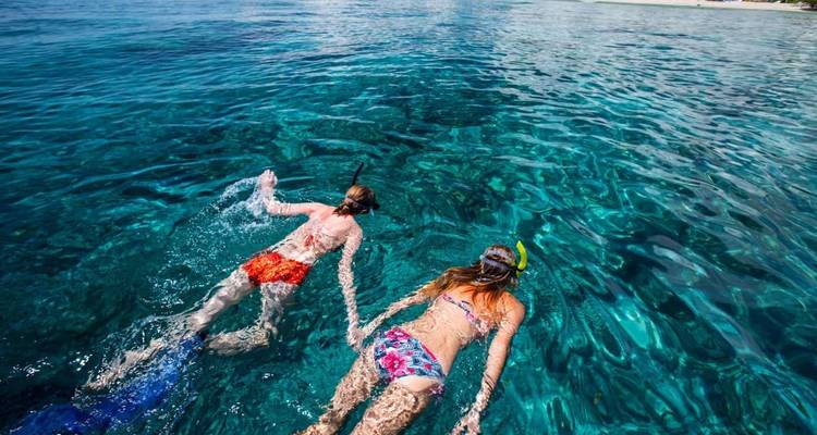 Twee mensen die snorkelen in helder blauw water.