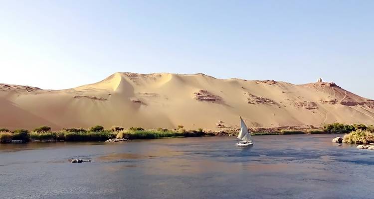 Una escena fluvial con un velero y dunas de arena en el fondo.