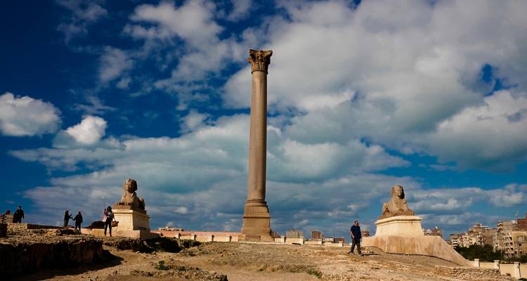 La Columna de Pompeyo de pie entre dos estatuas de esfinges en la cima de una colina con turistas cerca