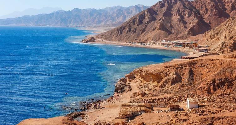 Ruwe, roodachtige bergen omzomen een diepblauw gat langs de Sinaïkust nabij Dahab.