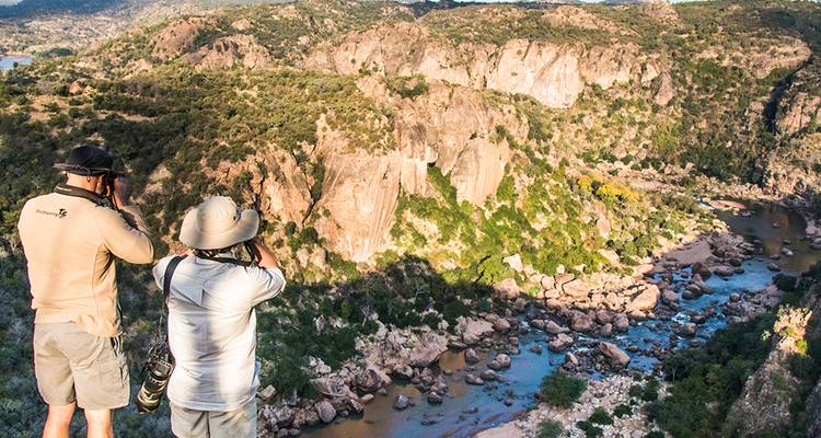 Twee natuurliefhebbers fotograferen een ruige canyon met een kronkelende rivier ver beneden.