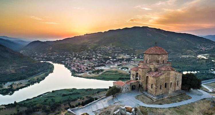 Vue aérienne d'une église avec une rivière et des montagnes au coucher du soleil.