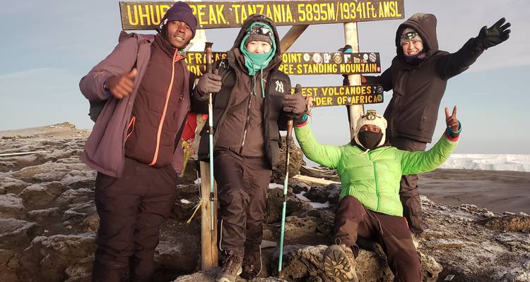 Groep bij het Uhuru Peak bord met berguitrusting.