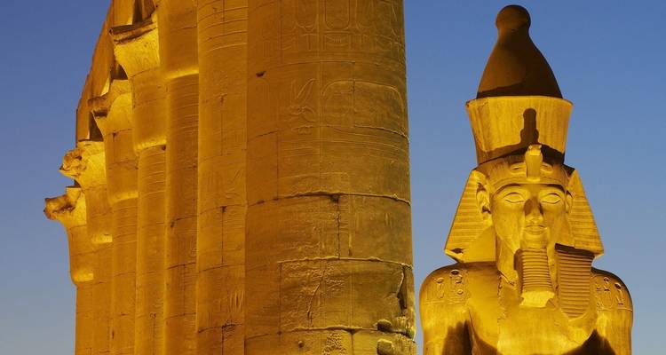 Illuminated ancient Egyptian statues and pillars at night.