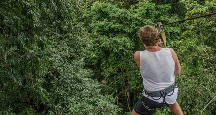 Een reiziger zoeft langs een jungle canopy zip line omringd door dicht groen bladerdak.
