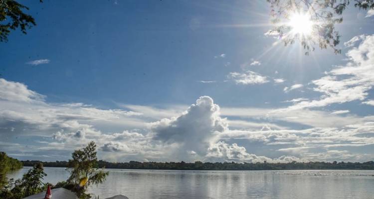 Felle zon en dramatische wolken weerspiegelen zich in een rustige jungle rivier of meer.