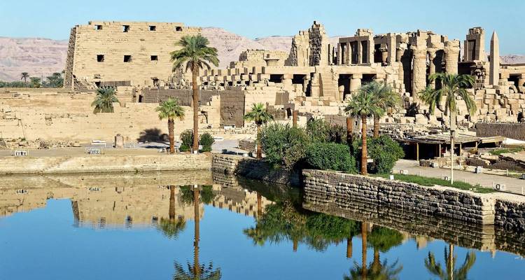 Ruines du temple de Karnak se reflétant dans un lac calme avec des montagnes désertiques au-delà.