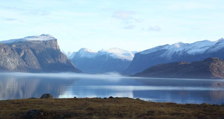 Un lac tranquille entouré de montagnes imposantes, partiellement voilé de brume.