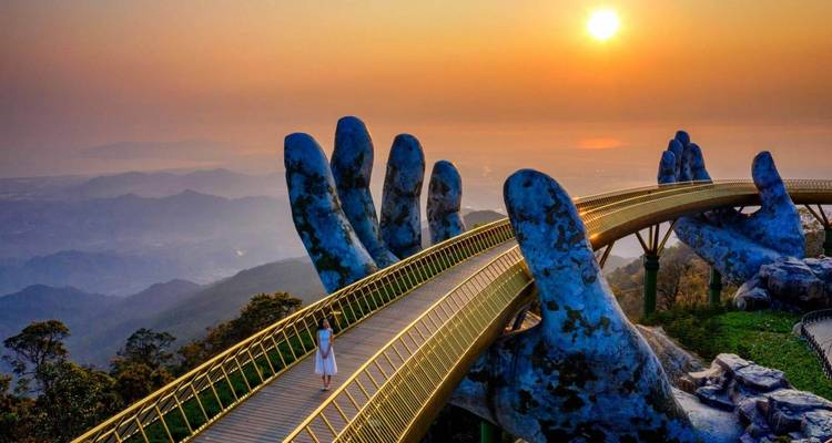 Gouden Brug met reuzenhanden bij zonsondergang, een persoon die erop loopt.
