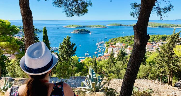 Overlooking a coastal town and garden from a hill, featuring a person with a hat.