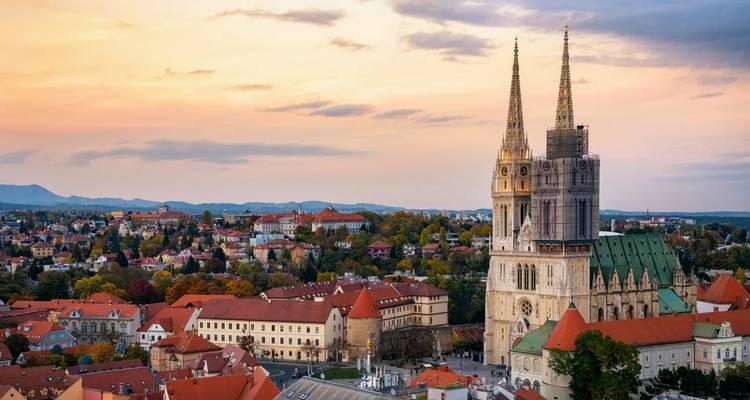 Cathedral with spires situated in a picturesque cityscape at sunset.