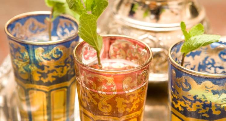 Nahaufnahme von verzierten marokkanischen Teegläsern gefüllt mit Minztee neben einer silbernen Teekanne.