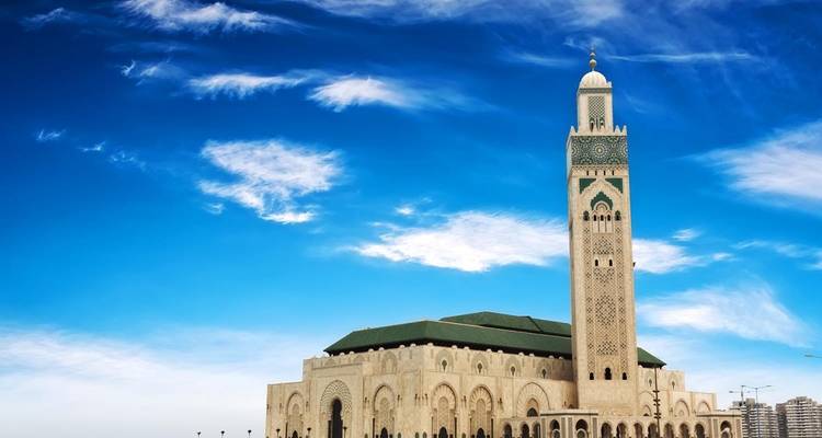 Die majestätische Hassan-II-Moschee steht vor einem leuchtend blauen Himmel mit zarten Wolken.
