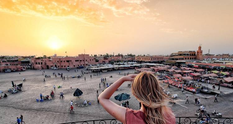 Sonnenuntergang über dem Platz Jemaa el-Fnaa in Marrakesch mit einem Reisenden, der auf die lebhafte Marktszene unten blickt.
