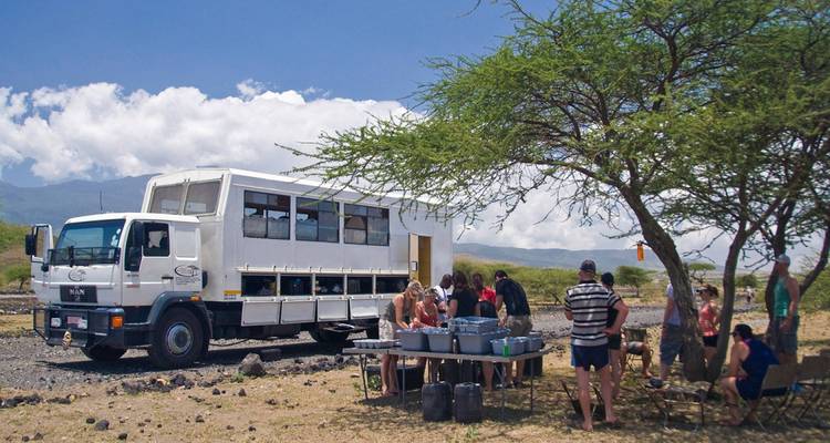Grupo de personas reunidas alrededor de una mesa al aire libre cerca de un camión grande.