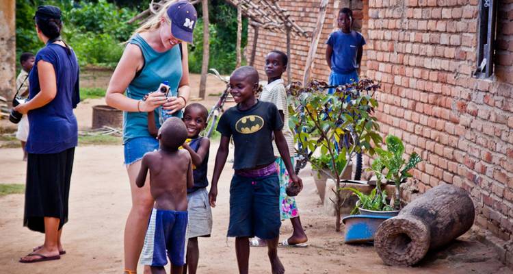 Grupo de niños y una mujer interactuando en un entorno de pueblo.