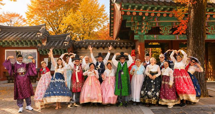 Grand groupe de touristes vêtus de hanbok colorés posant devant une porte de palais coréen ornée