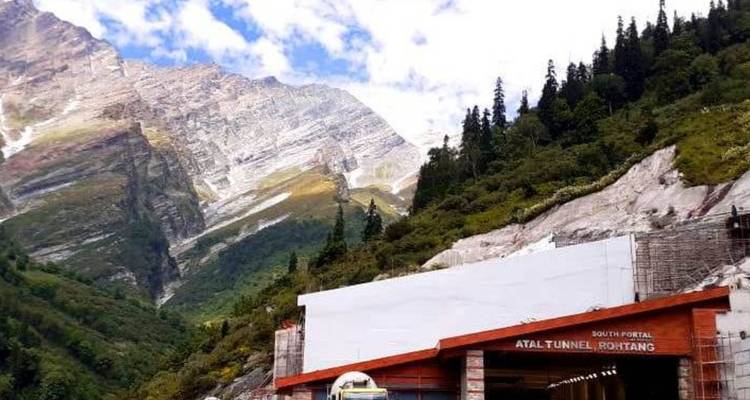 Entrance of Atal Tunnel Rohtang with towering rocky mountains and blue-sky backdrop.