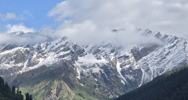 Snow-capped Himalayan peaks with clouds hugging the rugged ridges.