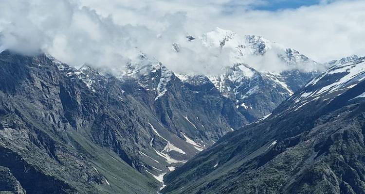 Deep alpine valley flanked by steep, snow-streaked mountain sides under a partly cloudy sky.