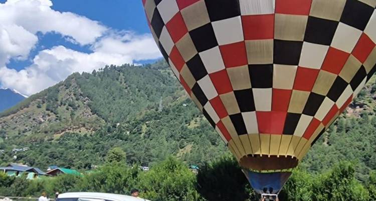 Checkerboard hot-air balloon preparing for takeoff against a hilly green backdrop.