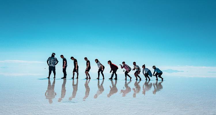 Una fila de viajeros posa en el espejo de las salinas de Uyuni, sus reflejos perfectamente visibles bajo un cielo azul vívido.