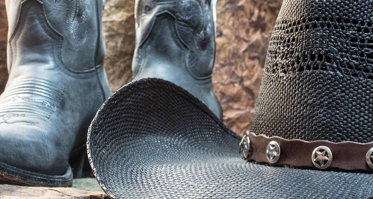 Still-life of western cowboy hat and rugged boots against rustic background