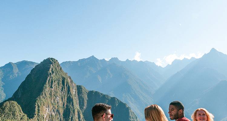 Amigos conversan en un mirador de Machu Picchu con Huayna Picchu y los Andes elevándose majestuosamente detrás.