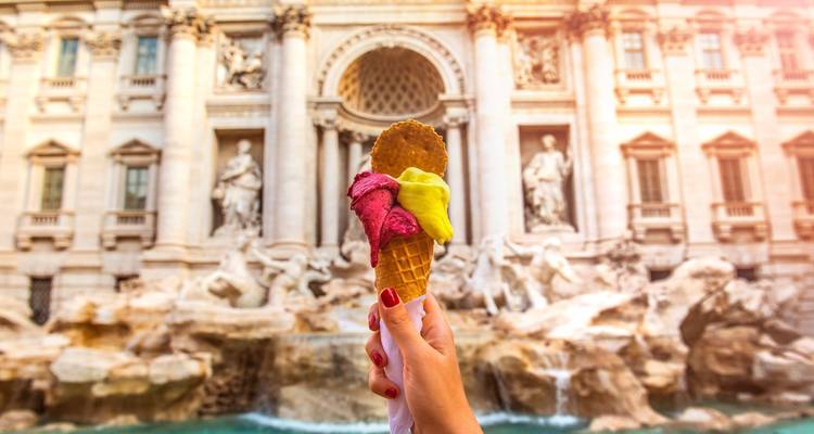 Close-up of an ice cream cone held up against the backdrop of a historic fountain.