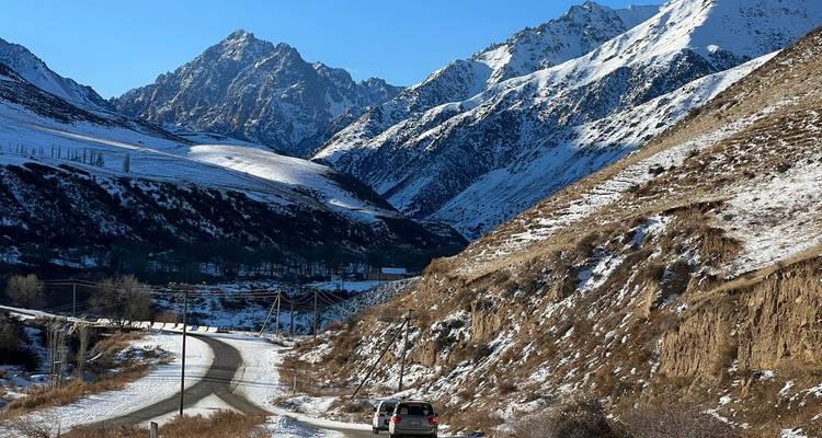 Snowy mountain landscape with a winding road and a vehicle.