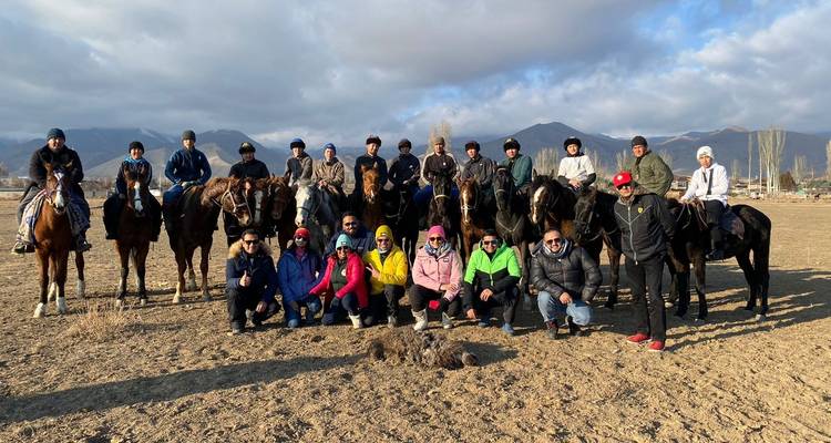 Large group of people and horses posing on a field with mountains in background.