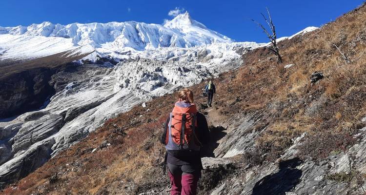 Randonneurs sur un sentier de montagne avec un sommet enneigé au loin.
