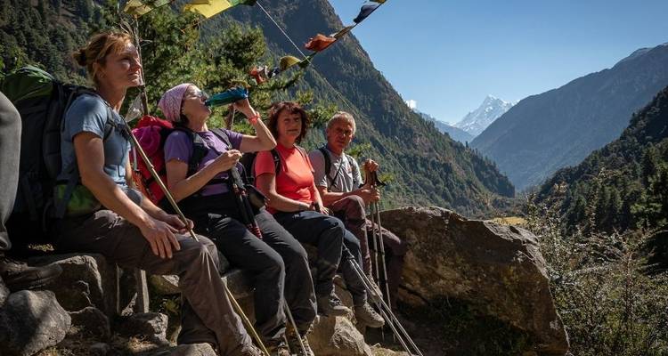 Randonneurs se reposant sous des drapeaux de prière avec vue sur les montagnes.