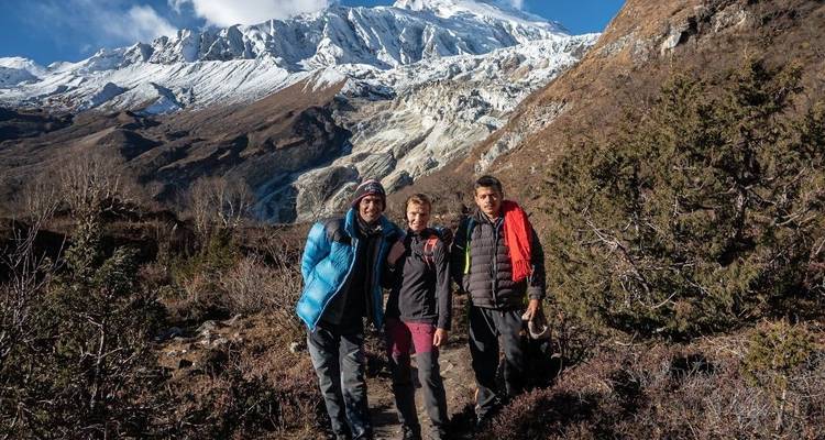 Trois randonneurs sur un sentier avec une montagne enneigée en arrière-plan.