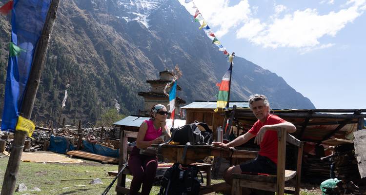 Deux randonneurs assis à un arrêt de repos rural en plein air avec des drapeaux de prières.