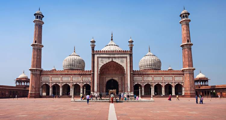 Die Jama Masjid mit Besuchern, die draußen spazieren, unter klarem Himmel.