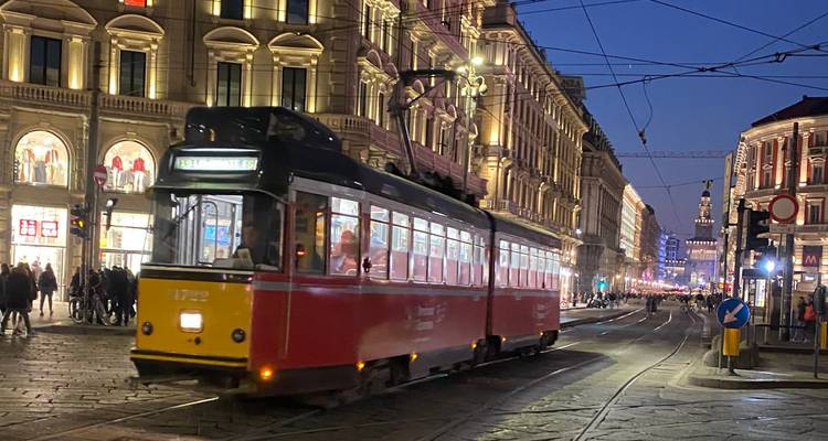 Eine Straßenbahn, die nachts durch eine belebte Straße in Mailand fährt.