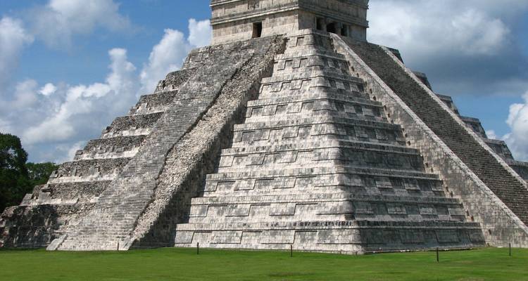Oude stenen piramide met trap in weelderige omgeving.