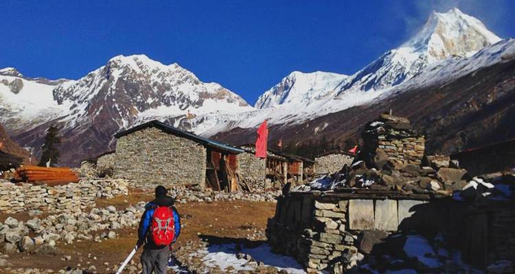 Person, die durch Steinhütten geht, mit schneebedeckten Gipfeln im Hintergrund.