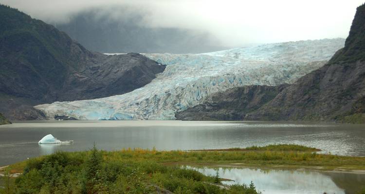 Glacier extending into a lake surrounded by steep cliffs.